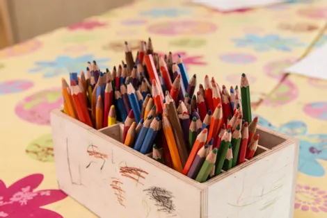 Box of colorful used pencils on floral tablecloth in a classroom or art space